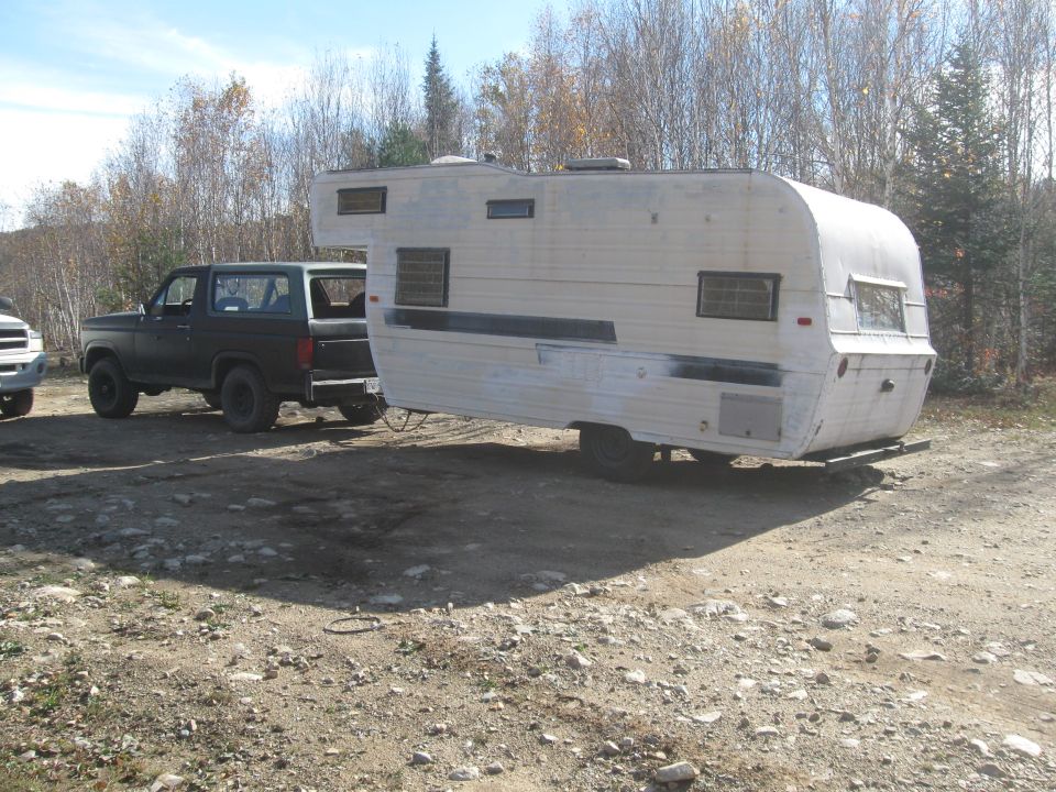 Dark colored Ford Bronco towing a white camper trailer on a dirt road
