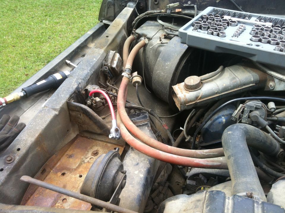 Engine bay with rusty metal, hoses, and a socket set on a tray
