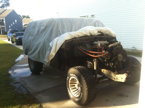 1979 Ford Bronco - A 1979 Ford Bronco is partially covered by a tarp, revealing its engine and off-road tires.
