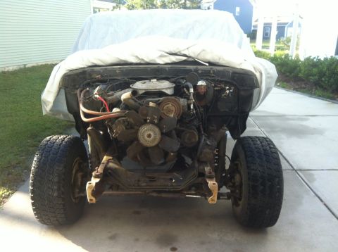 1979 Ford Bronco - The front end of a vehicle is covered by a car cover, revealing its engine and front tires.