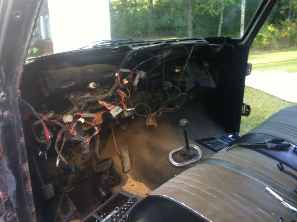 Vehicle interior with dashboard removed, exposing wiring and components. Gear shifter and part of a seat are visible