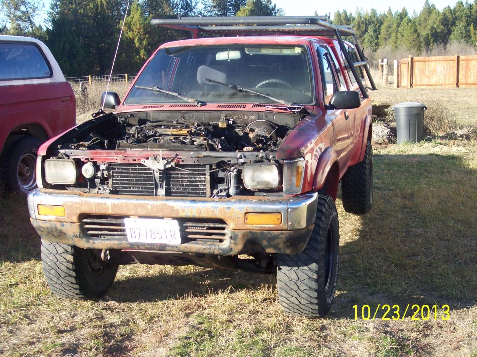 Red 1991 Toyota Pickup SR5 with hood open, rusty bumper, and roof rack