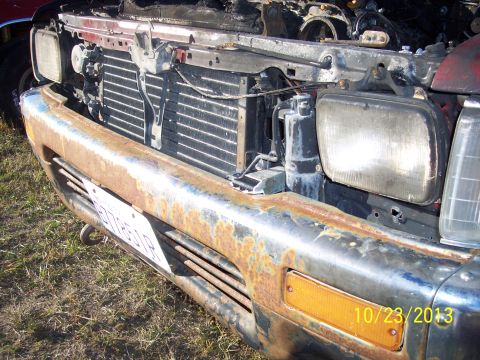 1991 Toyota Pickup/SR5 - The front end of a heavily rusted truck is shown with the hood open, revealing the radiator and headlights.