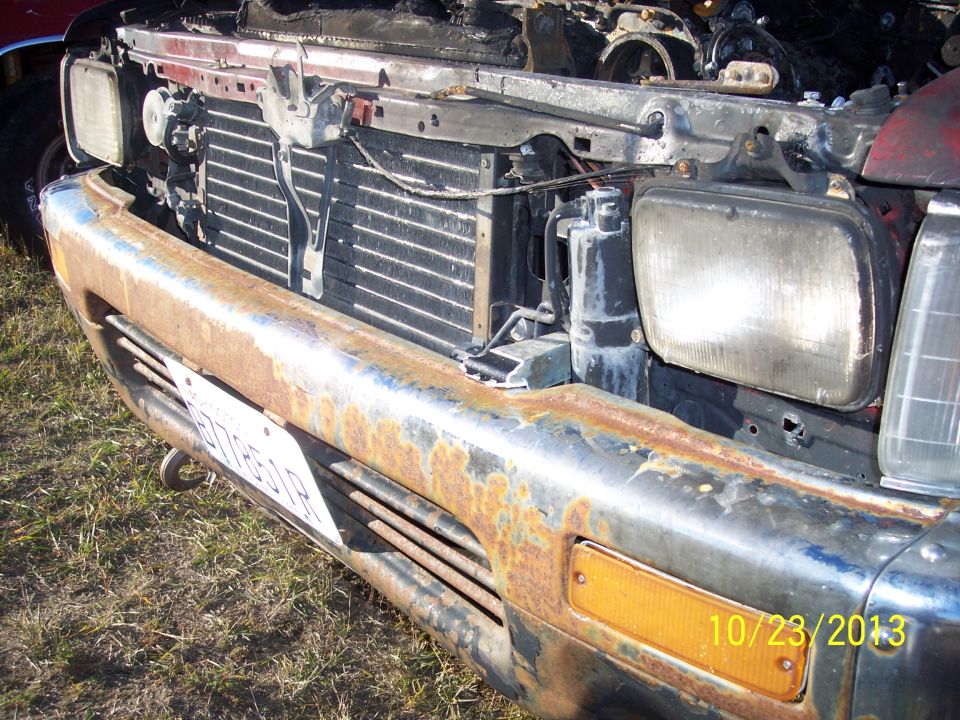 Rusty truck front with open hood, radiator, and headlights visible
