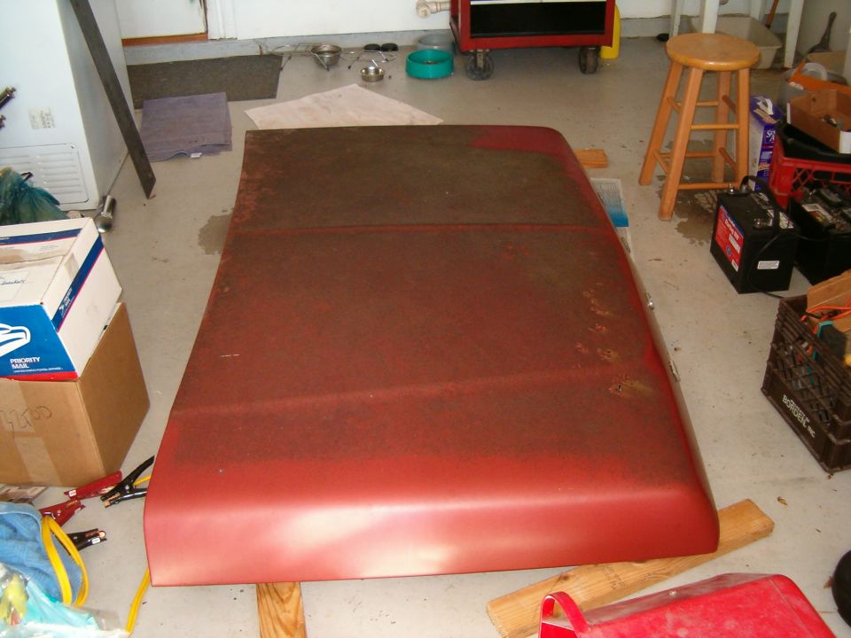 Red truck hood removed and laid upside down on the floor of a cluttered garage
