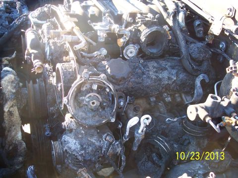 1991 Toyota Pickup/SR5 - The engine compartment of a vehicle shows extensive fire damage, with components blackened and obscured by debris.