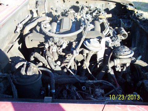 1991 Toyota Pickup/SR5 - The engine compartment of a red vehicle shows extensive fire damage with melted hoses and charred components.