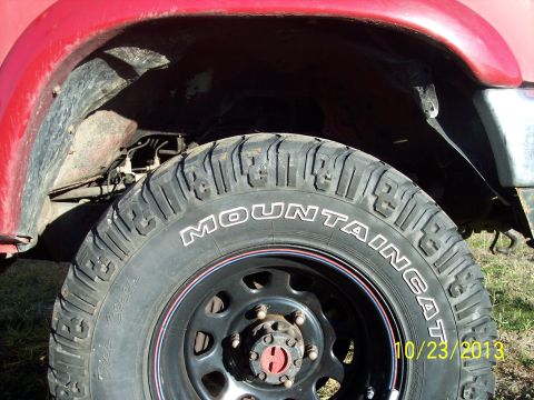 1991 Toyota Pickup/SR5 - Close-up view of a red truck's fender and tire, showing the 'MOUNTAIN CAT' tire branding.