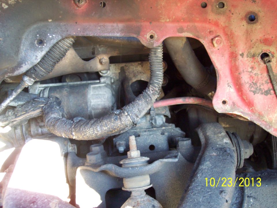 Close-up of engine bay with starter motor and hoses, red painted metal frame visible