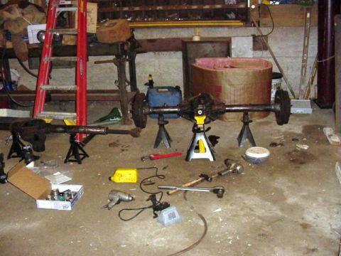 1992 Ford Bronco - Vehicle axles and various tools are laid out on the garage floor, suggesting a repair or rebuild project.