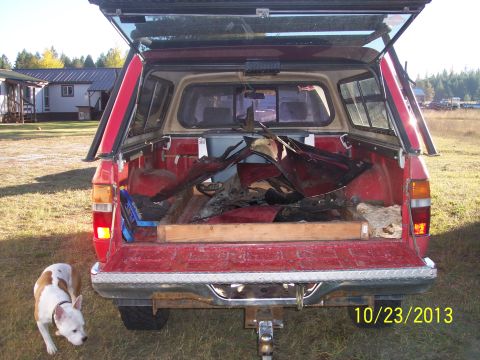 1991 Toyota Pickup/SR5 - Rear view of a red pickup truck loaded with debris, with a dog standing nearby.