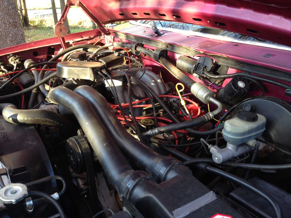 Engine bay of a red Ford truck, showing the V8 engine, hoses, and wiring