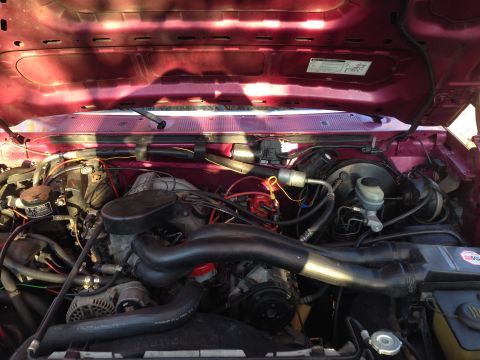 1992 Ford F-150 - The engine bay of a red 1992 Ford F-150 shows its V8 engine, complete with hoses and wiring.