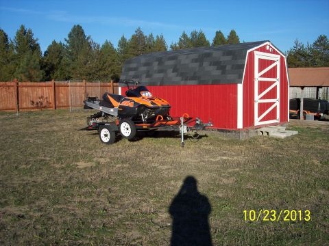 2004 Arctic Cat King Cat 900 - An orange and black snowmobile is parked on a trailer in front of a red barn on a sunny day.
