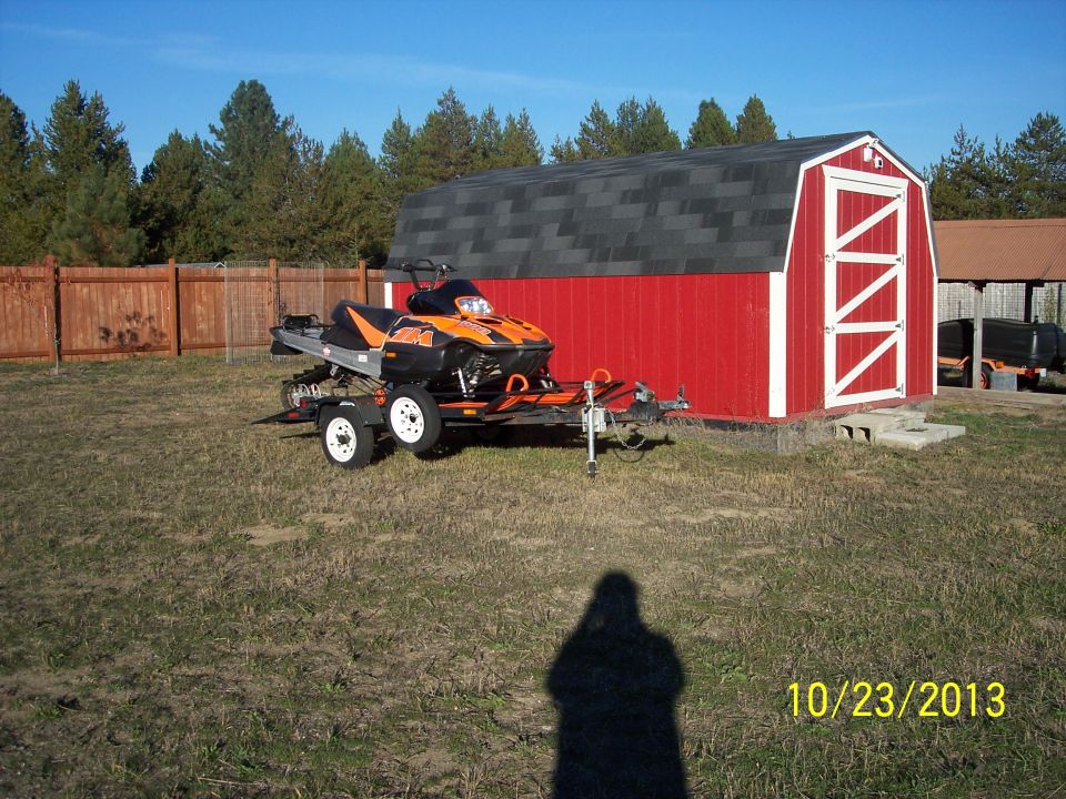 Orange and black snowmobile on a trailer in front of a red barn