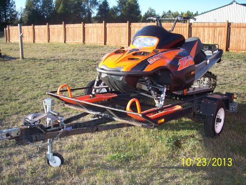 2004 Arctic Cat King Cat 900 - A snowmobile is parked on a trailer in a grassy area with a wooden fence in the background.