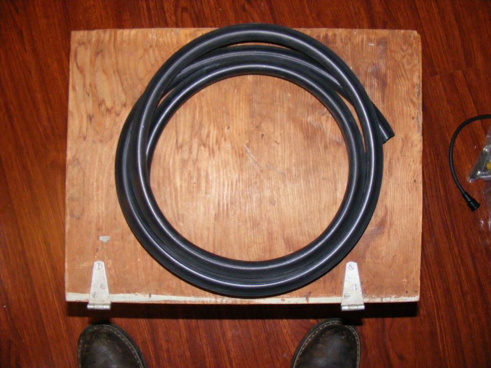 Coiled black rubber hose on a wooden board with hinges. Feet in dark shoes visible at bottom