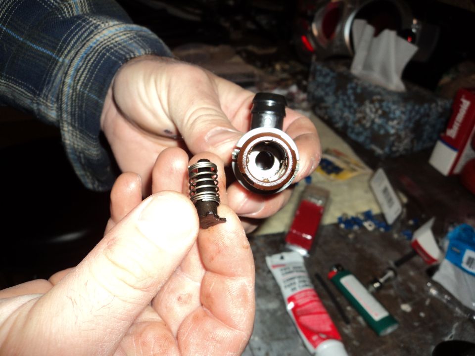 Hands holding a disassembled fuel line quick disconnect fitting, showing the spring-loaded valve and the housing