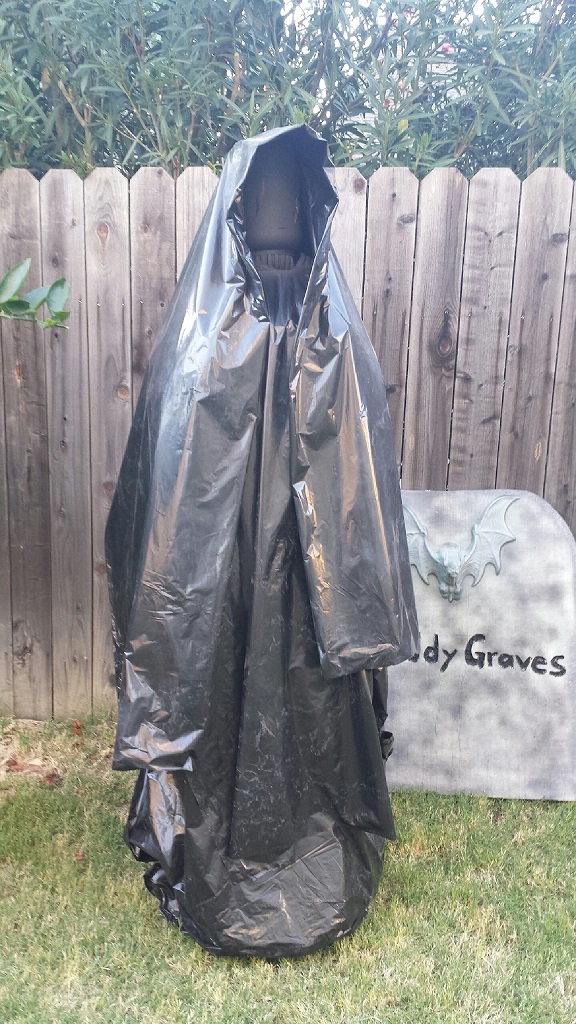 Grim reaper Halloween decoration in front of a wooden fence and a tombstone prop that reads 'Bloody Graves'