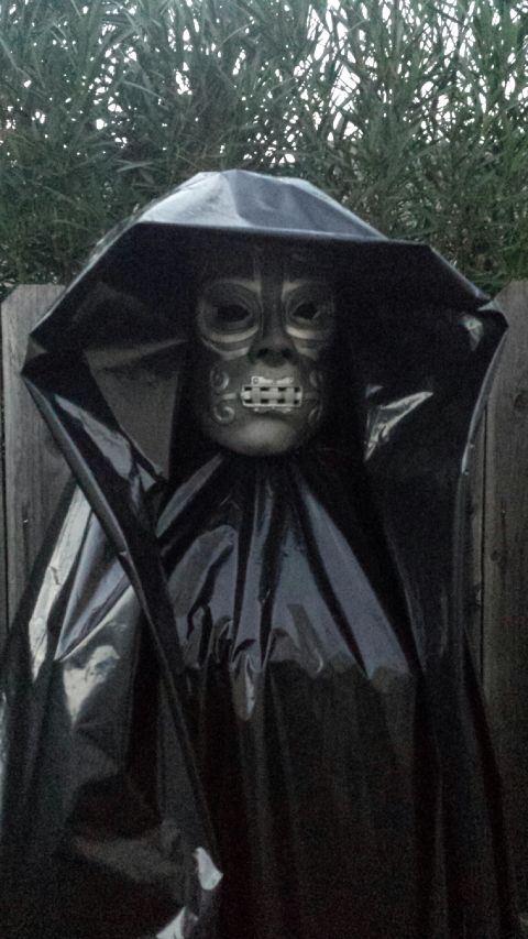 1989 Ford Bronco - A figure resembling a Death Eater from Harry Potter stands outdoors, shrouded in a black cloak and wearing a distinctive skull mask.