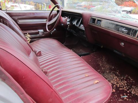 1991 Ford LTD Crown Victoria - Interior view of a car with a maroon bench seat and cracked windshield, showing debris on the floor.
