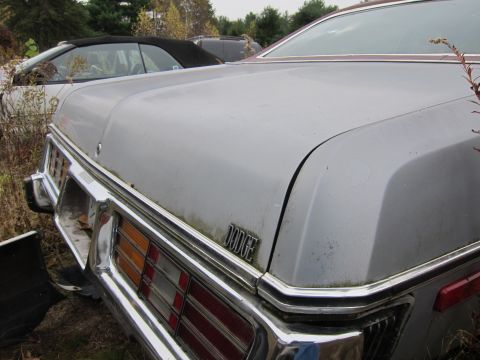 1991 Ford LTD Crown Victoria - A silver Dodge car sits in a junkyard, showing its rear end and chrome bumper.