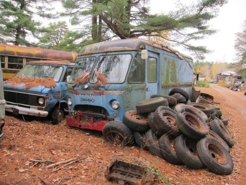 1991 Ford LTD Crown Victoria - A blue step van, marked DH460, sits in a junkyard next to other vehicles and a pile of tires.