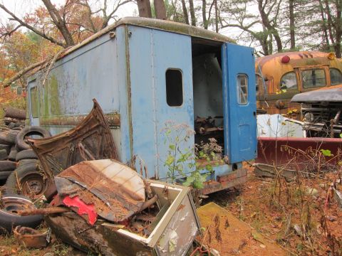 1991 Ford LTD Crown Victoria - Junkyard scene with an old step van and a school bus among debris and trees.