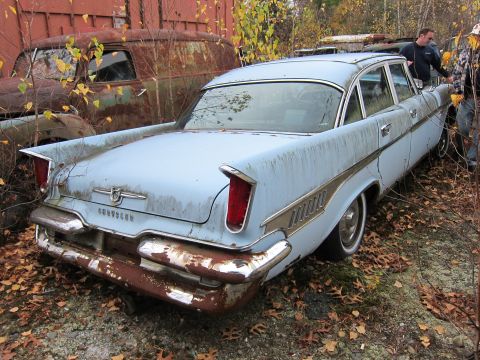 1991 Ford LTD Crown Victoria - A light blue sedan with distinctive tail fins and chrome trim sits in a junkyard, surrounded by fallen leaves and other derelict vehicles.