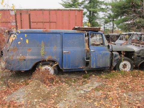 1991 Ford LTD Crown Victoria - A dilapidated blue panel van sits abandoned in a junkyard, surrounded by debris and other vehicles.