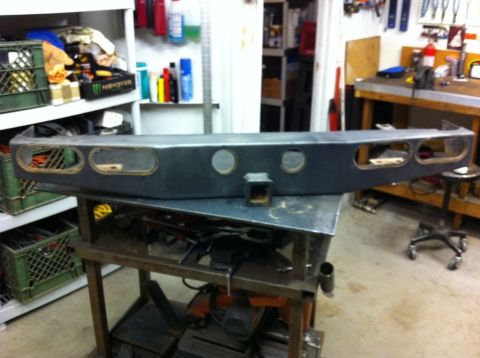 1987 Suzuki Samurai - Aftermarket rear bumper with hitch receiver, gray metal, oval cutouts, circular cutouts, on workbench.
