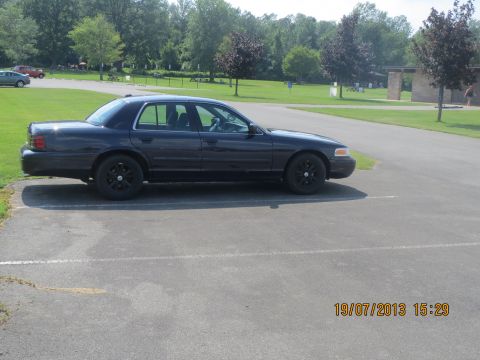 2003 Ford Crown Victoria - Side view of a dark 2003 Ford Crown Victoria sedan parked in a lot on a sunny day.