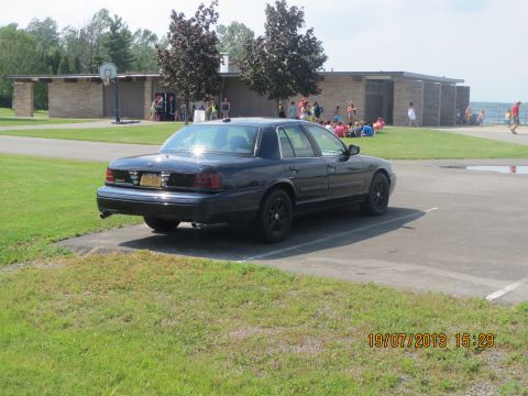 2003 Ford Crown Victoria - Black 2003 Ford Crown Victoria parked near a building with people in the background.