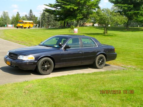 2003 Ford Crown Victoria - A dark blue 2003 Ford Crown Victoria sedan is parked on a driveway with a yellow school bus in the background.