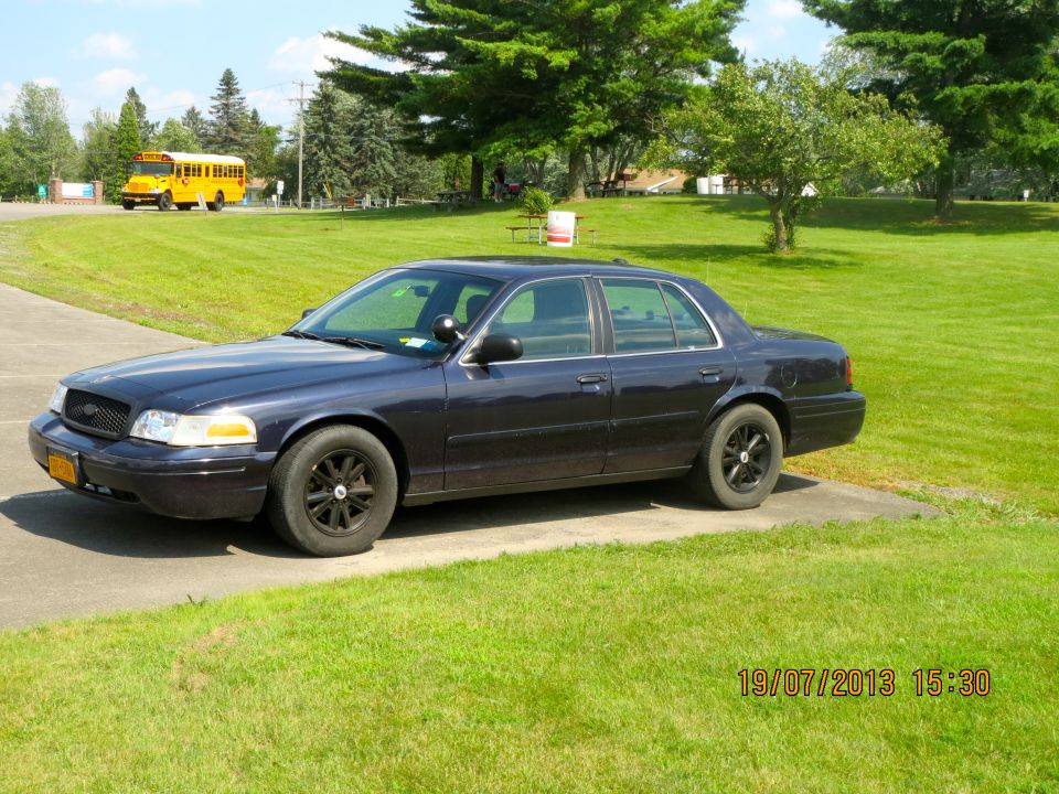 Dark blue 2003 Ford Crown Victoria sedan parked on a concrete driveway, black wheels, slight damage on front bumper