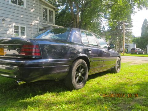 2003 Ford Crown Victoria - A dark sedan sits on a grassy lawn next to a house, with another vehicle in the distance.