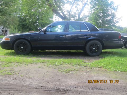 2003 Ford Crown Victoria - A dark blue 2003 Ford Crown Victoria is seen from the side, parked on a grassy area.