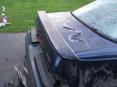 1996 Ford Bronco - The rear of a dark blue car features a spoiler and 'Turbo Coupe' badging, with visible paint damage.