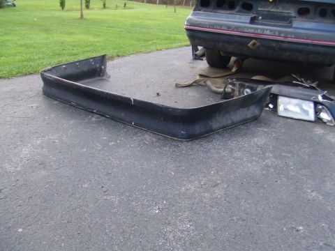 1996 Ford Bronco - A detached car bumper and headlight lie on the ground next to a vehicle being worked on.