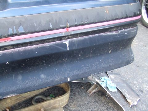 1996 Ford Bronco - The rear bumper of a vehicle shows significant wear and damage, with a tow strap underneath.