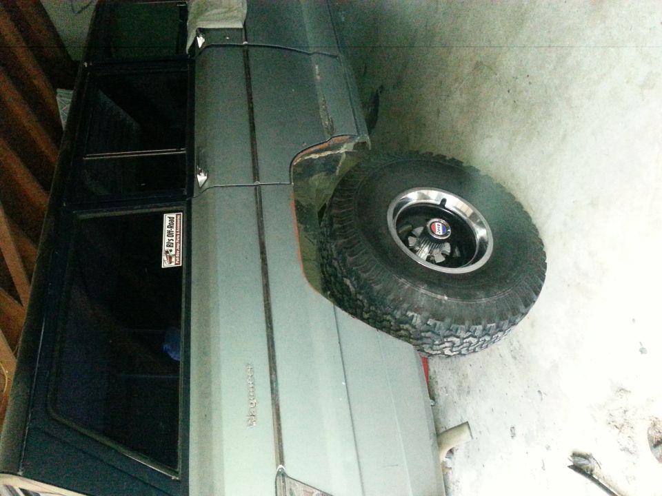 Side view of a light-colored Jeep Grand Wagoneer with a sticker on the rear window. Spare tire is visible
