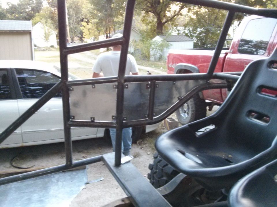 Off-road buggy interior with roll cage and racing seat, red pickup truck visible