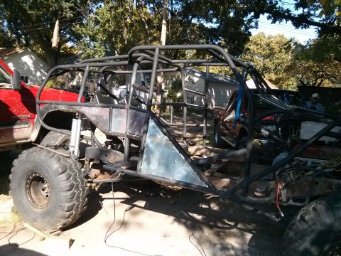 1986 Ford Bronco - This custom-built off-road buggy features a prominent roll cage and oversized tires, seen alongside another vehicle.