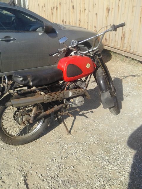 1991 Ford Bronco - A red motorcycle with a black seat and exhaust is parked next to a gray car.