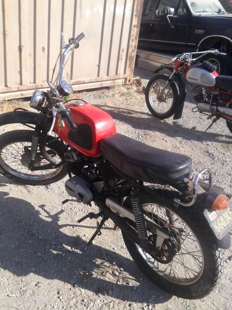 1991 Ford Bronco - A red motorcycle is parked outdoors next to another motorcycle, with a large metal gate in the background.
