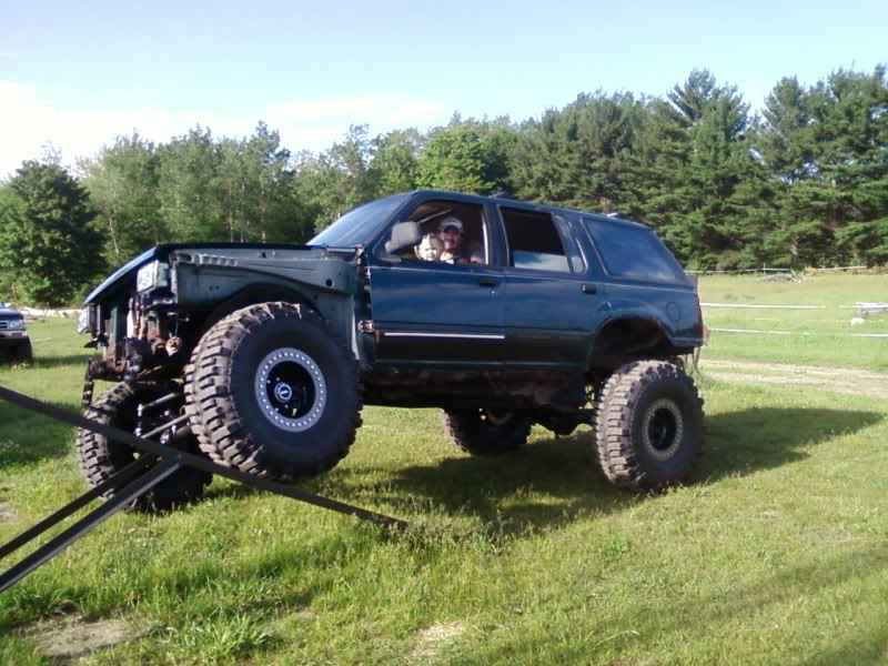 Modified dark green SUV with large tires and lifted suspension on a grassy field.