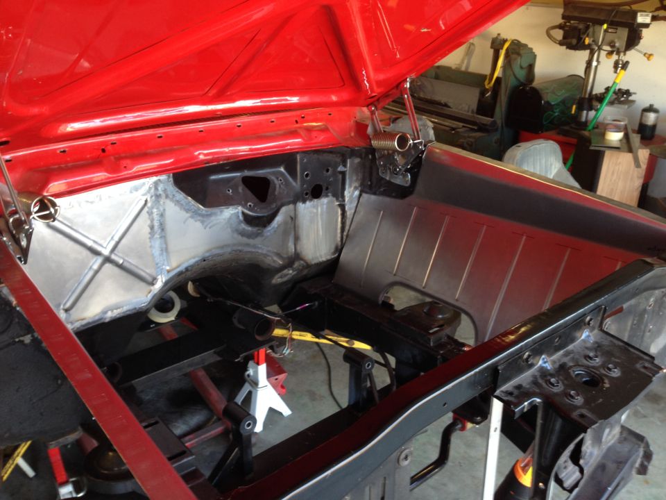 Classic red car engine bay with custom metalwork on firewall and inner fenders.
