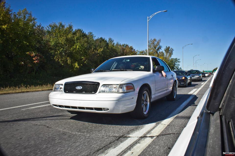 White Ford Crown Victoria sedan in traffic on a sunny day.