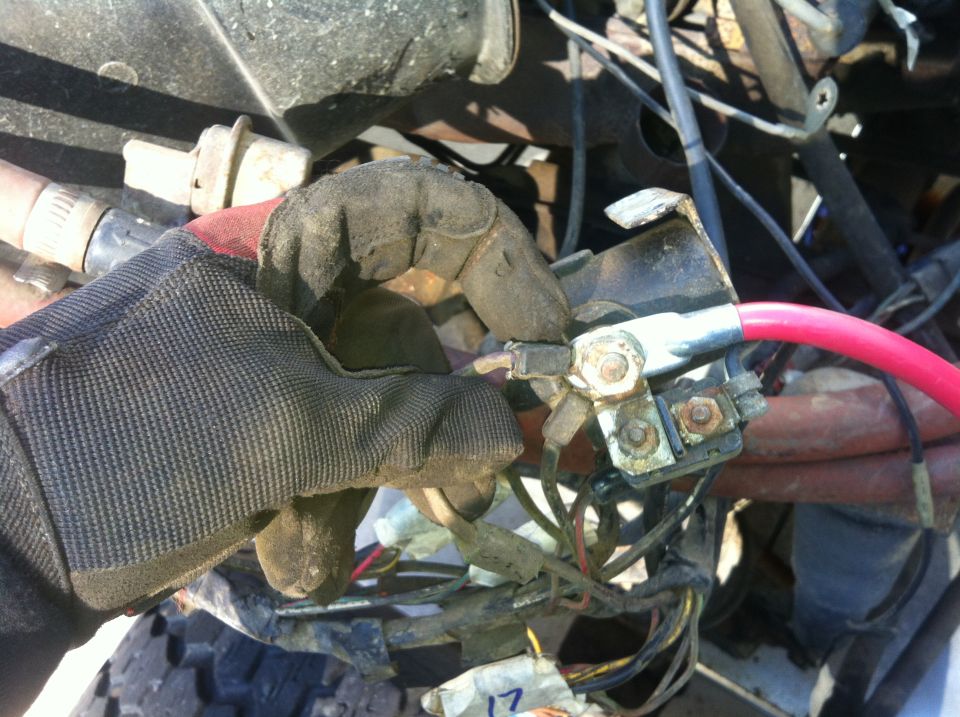 Gloved hand connecting red battery cable to terminal block with wires.