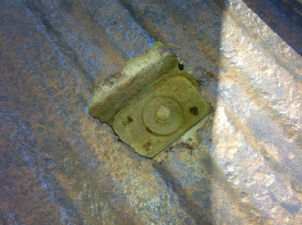 Close-up of rusted corrugated metal with a bracket and bolt assembly.